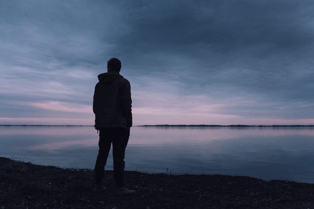 a man's silhouette looking out over a calm lake during sunset